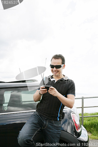 Image of Happy man using his mobile outside his car