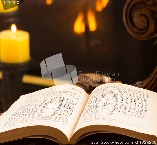 Image of Paperback book open on chair by fire and candle