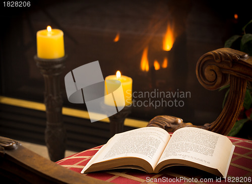 Image of Paperback book open on chair by fire and candle