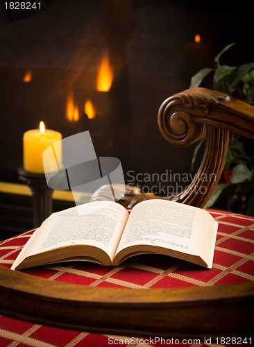 Image of Paperback book open on chair by fire and candle