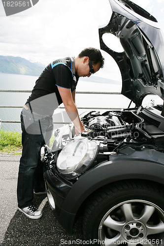 Image of A young man fixing his car up the hills