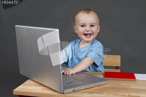 Image of baby with laptop computer in grey background
