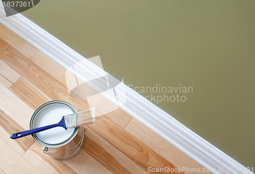 Image of Paintbrush and an open can of white paint on wooden floor