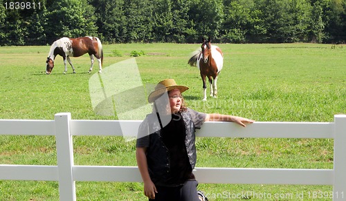 Image of Young boy leaning on fence wtih two horses in background