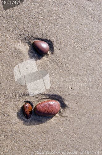 Image of Colored stones on wet beach sand rinsed by waves. 