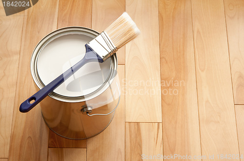 Image of Paintbrush and a can of white paint on wooden floor