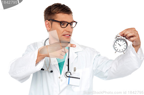 Image of Shocking young doctor pointing at alarm clock