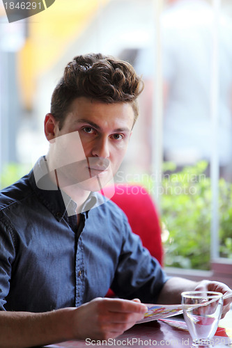 Image of Young handsome man in restaurant looking at menu