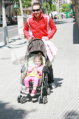 Image of Happy father smiling with his daughter in baby carriage