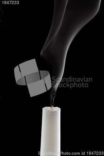 Image of White candle with smoke on black background.