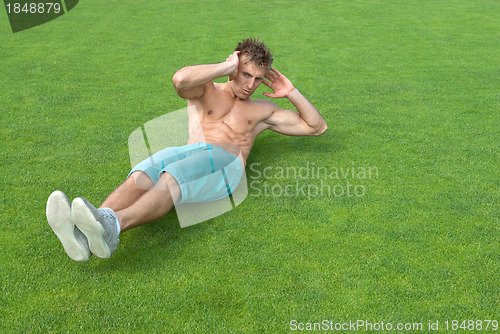 Image of Young man doing sit-ups on green grass