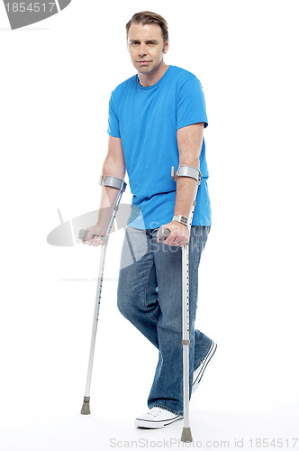 Image of Painful expression by young man walking with help of crutches