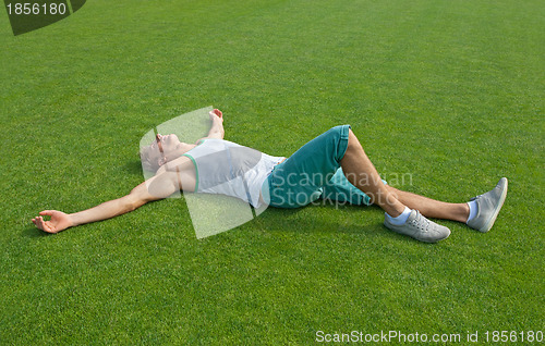 Image of Sporty guy relaxing on green training field