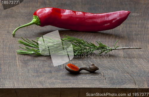 Image of Fresh red pepper, sprig of rosemary, wooden measuring spoon of g