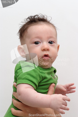 Image of Cute serious baby held by his mother turns toward the camera