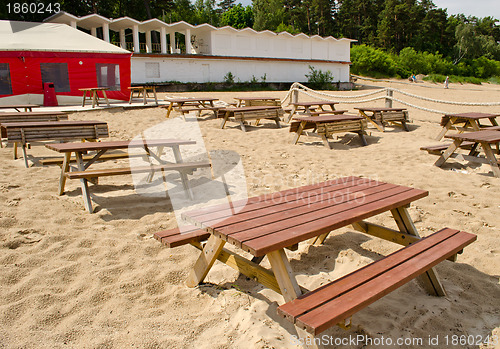 Image of Wooden tables and benches surrounded by sea sand and huge cafe tent. 