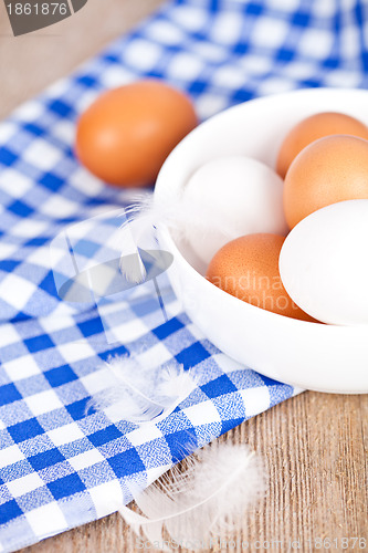 Image of eggs in a bowl, towel and feathers on rustic wooden table