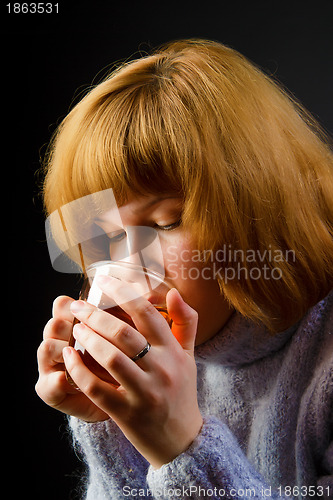 Image of girl in a sweater on a black background drinking tea