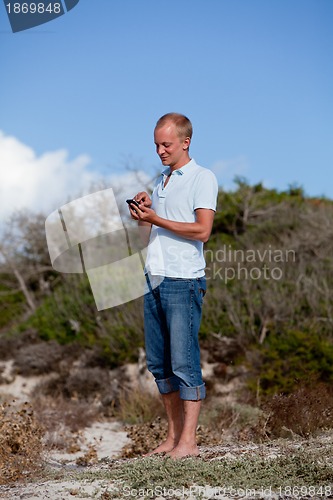 Image of young man outside in summer on beach with mobile phone