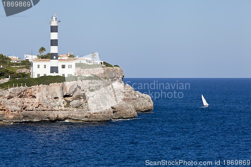 Image of white lighthouse on rocks in the sea ocean water sky blue