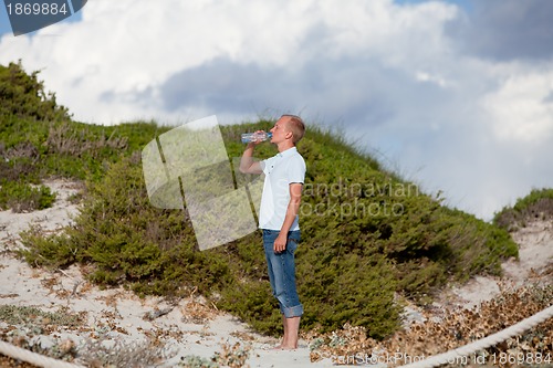 Image of young man ist drinking water summertime dune beach sky