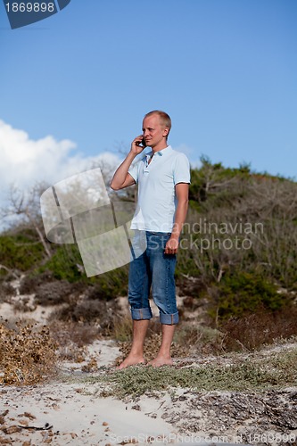 Image of young man outside in summer on beach with mobile phone