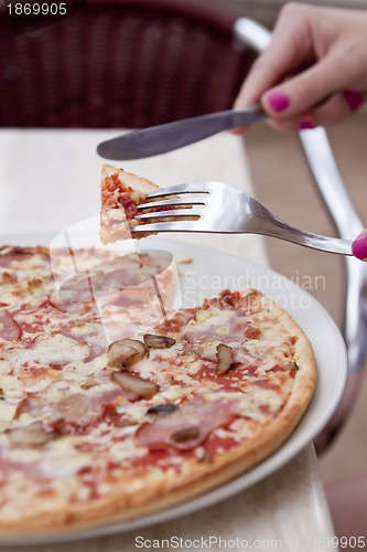 Image of young woman is eating a pizza in restaurant