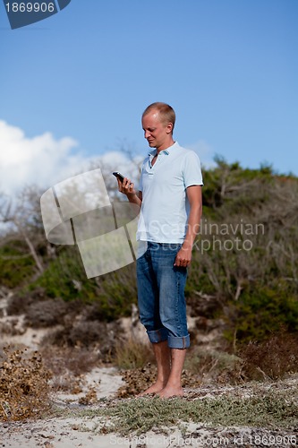Image of young man outside in summer on beach with mobile phone