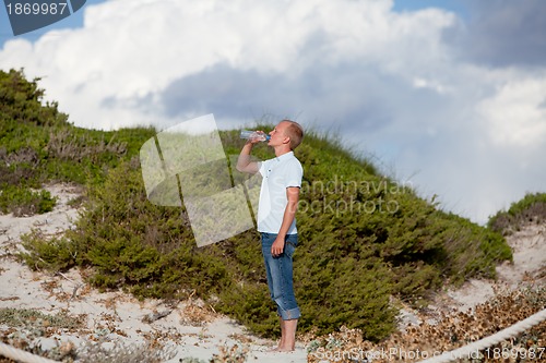 Image of young man ist drinking water summertime dune beach sky