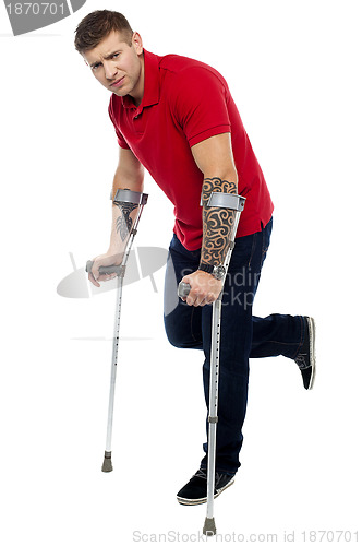 Image of Painful expression of young guy walking with help of crutches