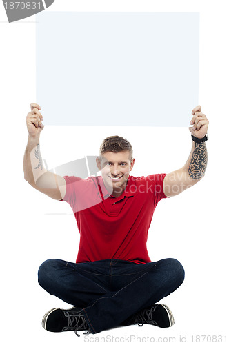 Image of Casual man sitting on floor with billboard raised above head