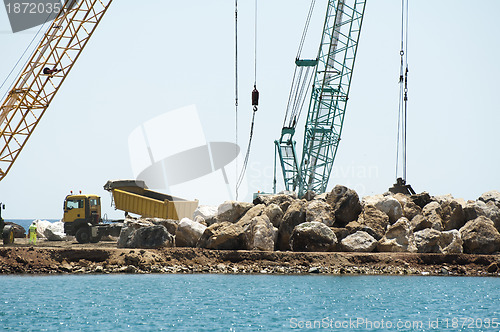 Image of Building a dike. Cranes and excavator put stones