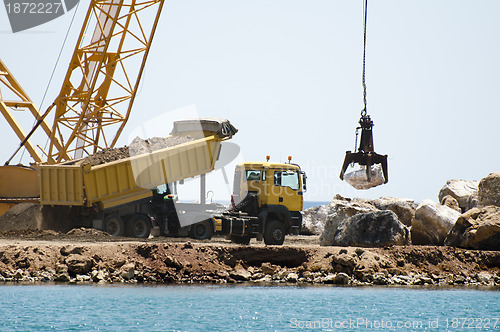 Image of Building a dike. Cranes and excavator put stones