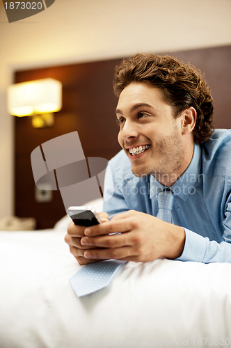 Image of Man holding cellphone and lying on bed, relaxed