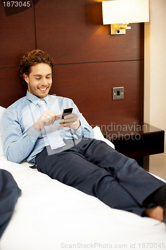 Image of Man resting in luxurious bed and messaging