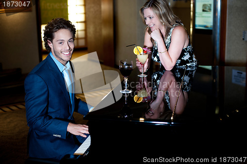 Image of Man playing piano and entertaining his companion holding cocktail