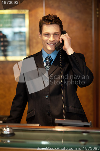 Image of Cheerful front desk executive attending phone call