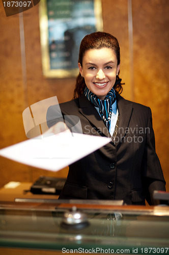 Image of Cheerful female receptionist offering check-in papers
