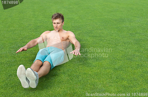 Image of Young man doing sit-ups on sports field