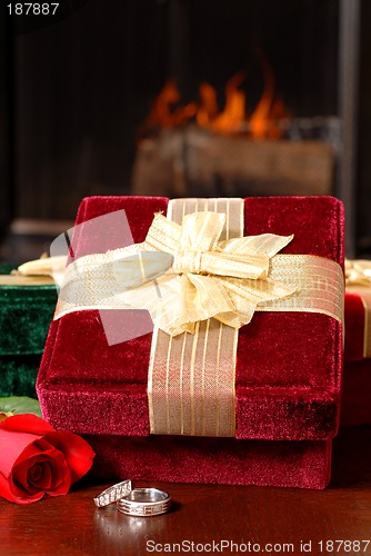 Image of Wedding rings with Christmas gifts and a rose in front of a fire