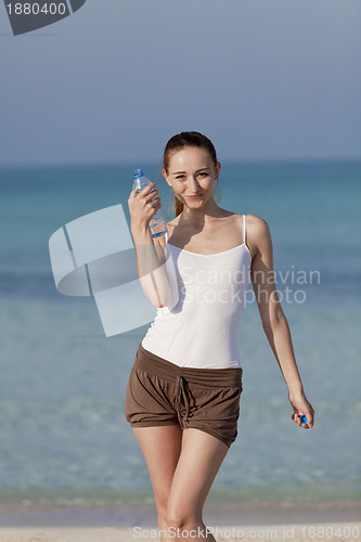 Image of Woman drinking water from a bottle on the beach portrait