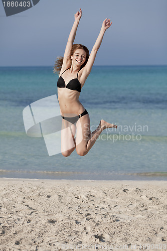 Image of Woman with bikini jumping happily on the beach portrait