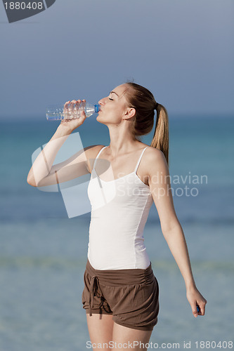 Image of Woman drinking water from a bottle on the beach portrait