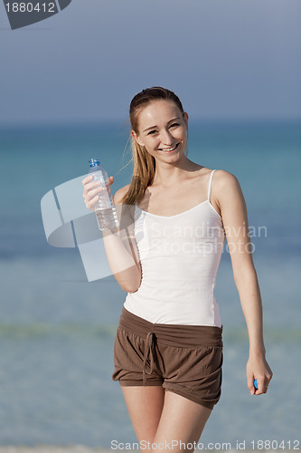 Image of Woman drinking water from a bottle on the beach portrait