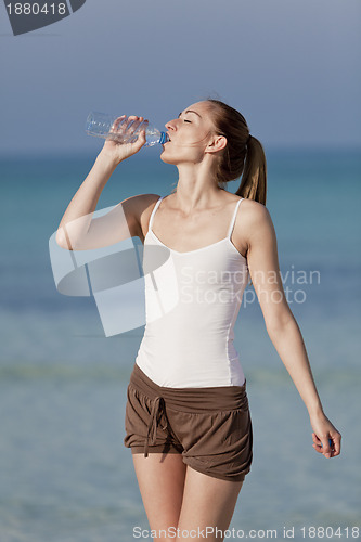 Image of Woman drinking water from a bottle on the beach portrait