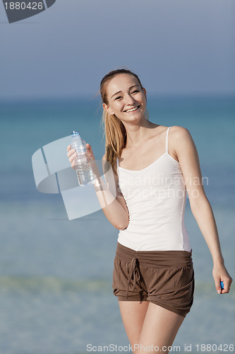 Image of Woman drinking water from a bottle on the beach portrait