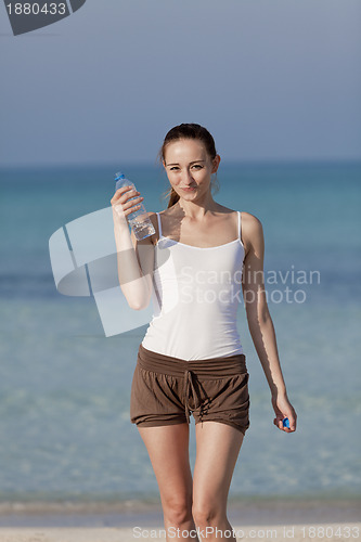 Image of Woman drinking water from a bottle on the beach portrait