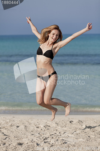 Image of Woman with bikini jumping happily on the beach portrait