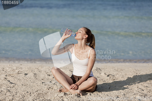 Image of Woman drinking water from a bottle on the beach landscape