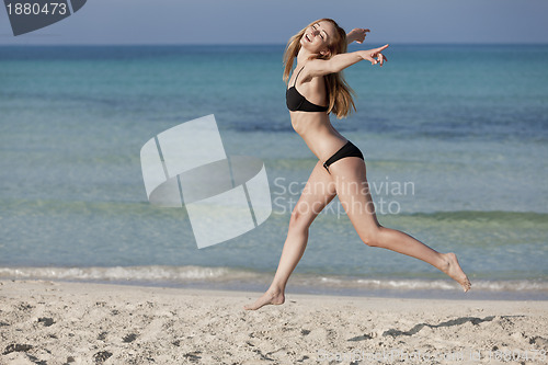 Image of Woman with bikini jumping happily on the beach landscape